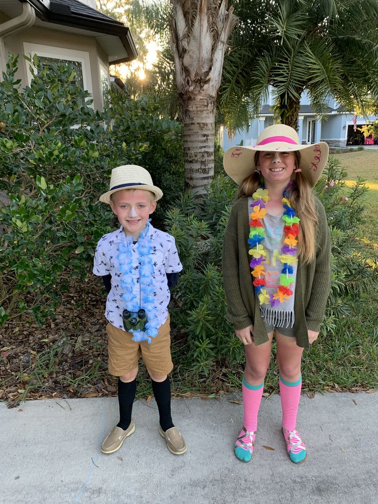 two children wearing hats and scarves standing next to each other in front of a palm tree