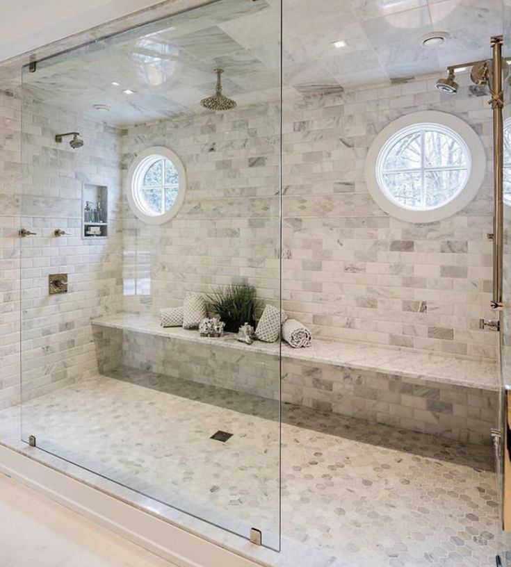 a bathroom with a large glass shower door and white marble tile walls, along with two round windows