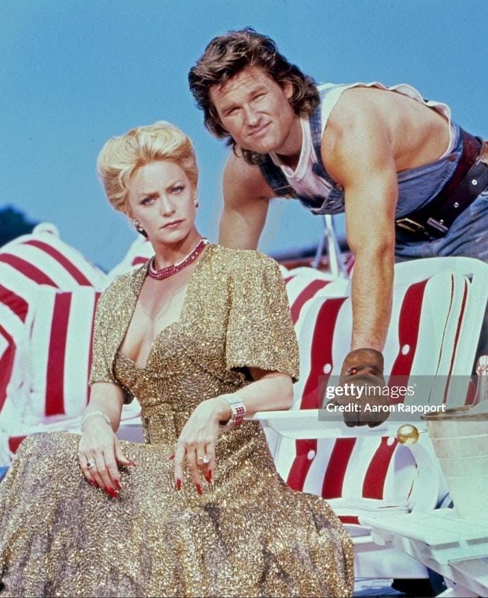 two people sitting on beach chairs in front of umbrellas, one is leaning over the other