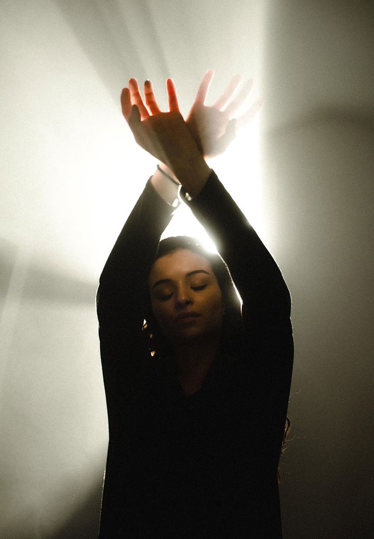 a woman is holding her hands up in the air with light shining on her face