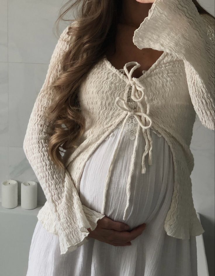 a pregnant woman with her hands on her belly, wearing a white dress and long sleeves