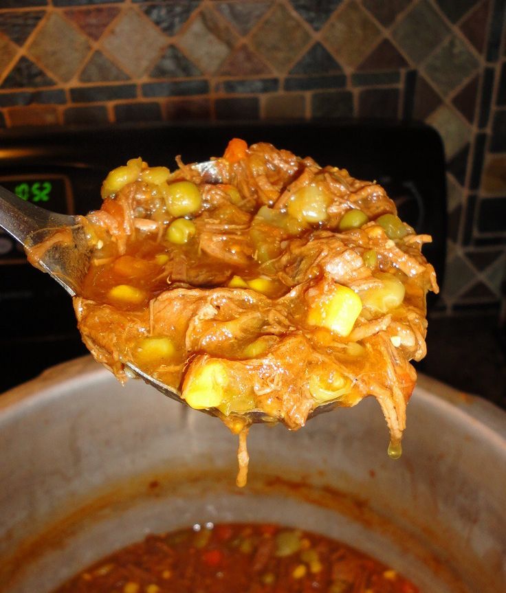 a spoon full of food sitting on top of a pot filled with chili and corn