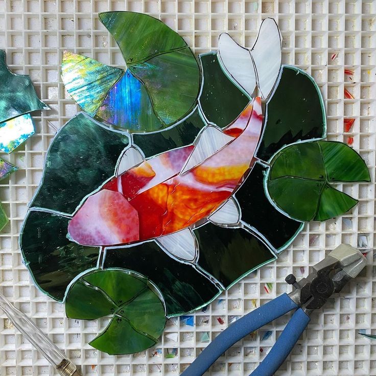 a fish made out of stained glass sitting on top of a table next to pliers