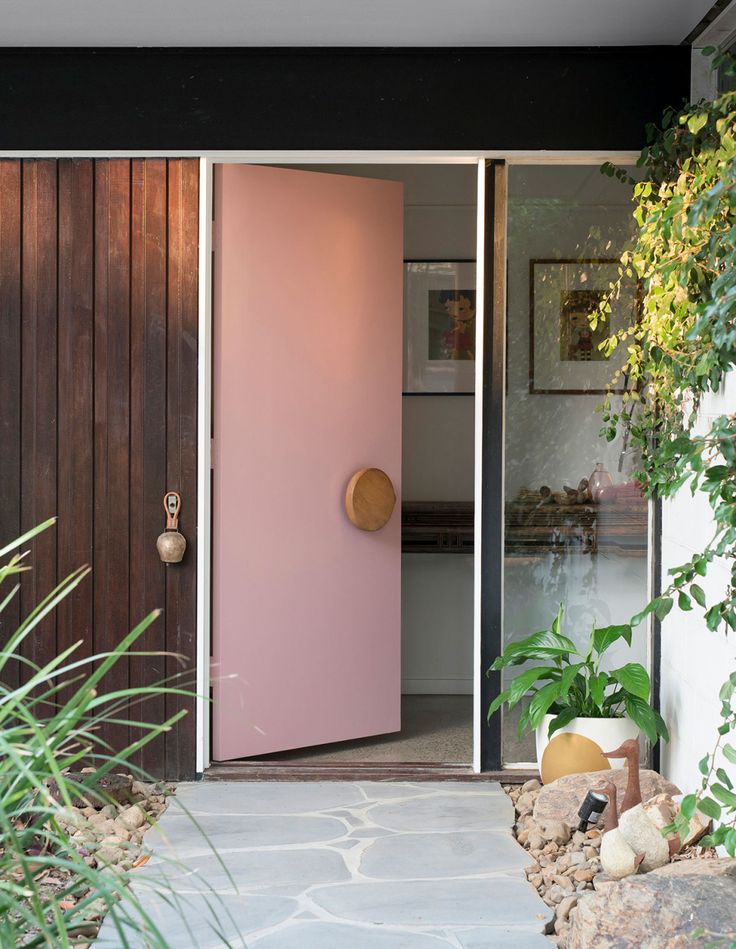 a pink door in front of a house with plants and rocks on the side walk