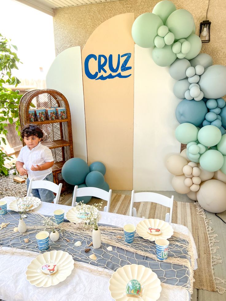 a little boy sitting at a table in front of some balloons