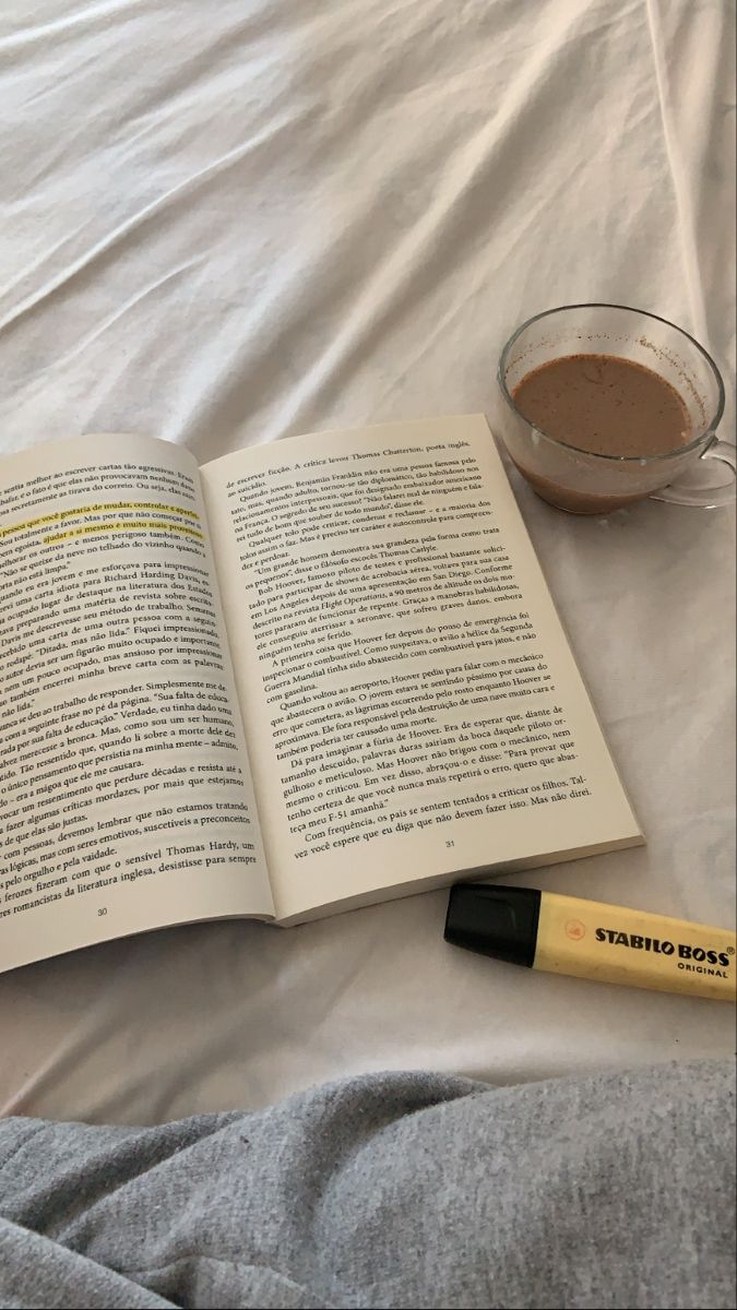 an open book sitting on top of a bed next to a cup of coffee