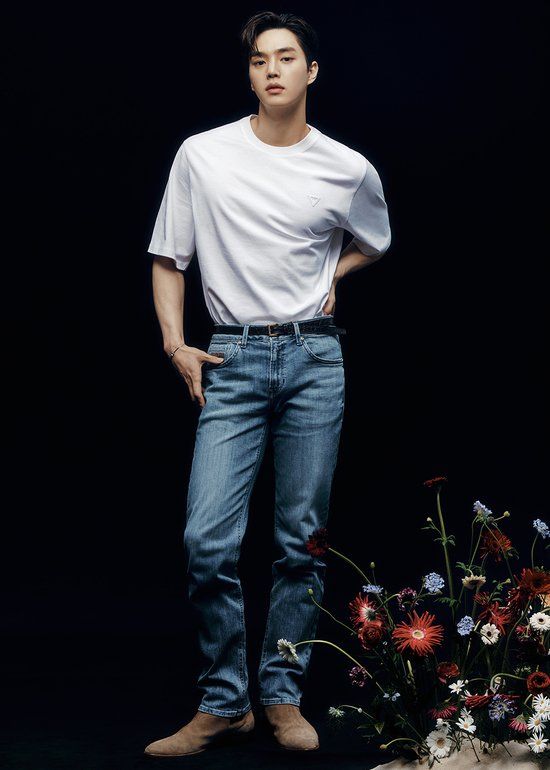 a man standing next to a bunch of flowers in front of a black background with his hands on his hips