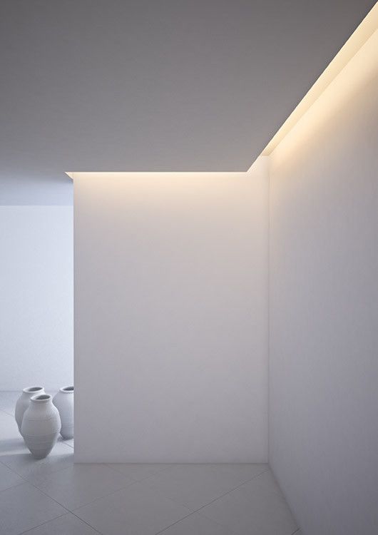 an empty white room with two vases on the floor and light coming in from the ceiling