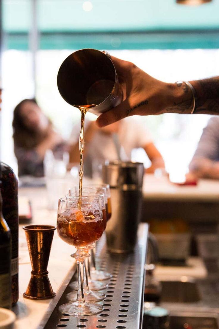 a person pours some liquid into glasses on a bar with other people in the background