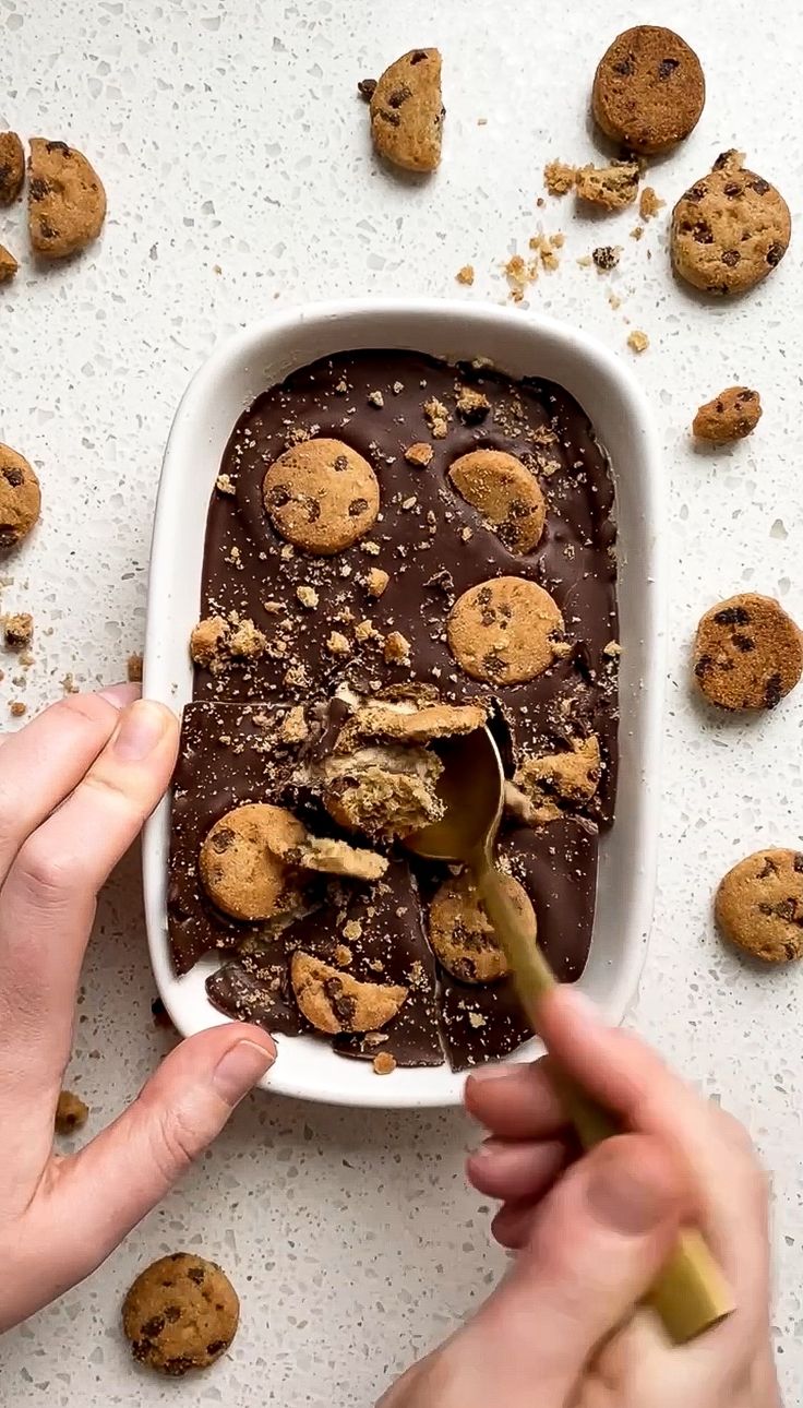 a person scooping chocolate into a dish with cookies on the side