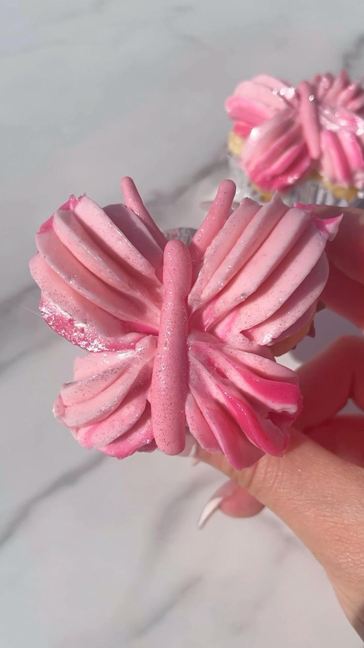 a hand holding two pink cupcakes with icing on them