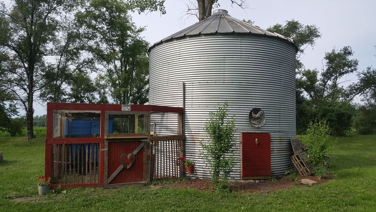 a large metal silo sitting in the middle of a field next to a tree