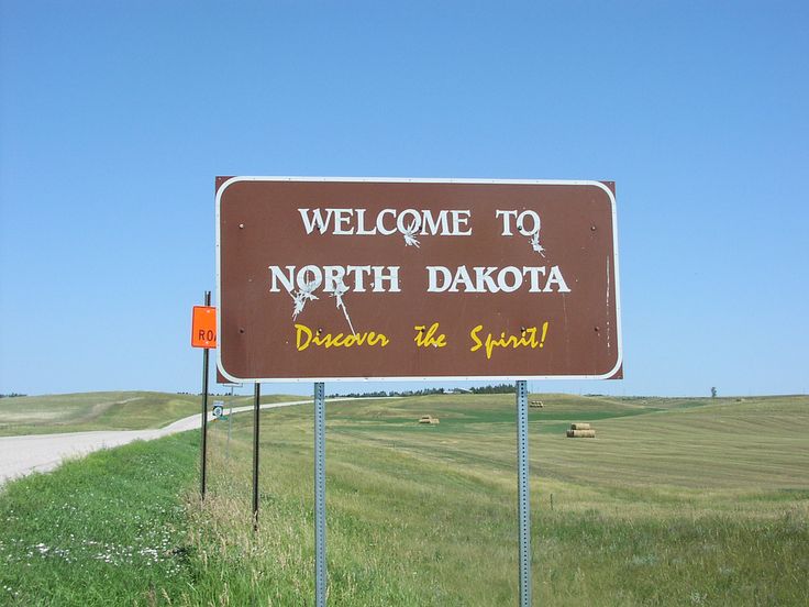 a welcome sign to north dakota is posted on the side of a road in an open field