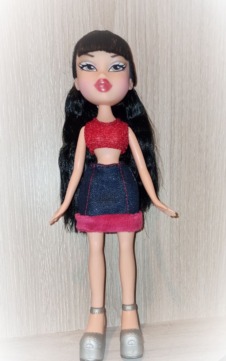 a close up of a doll with long black hair wearing a red top and blue skirt