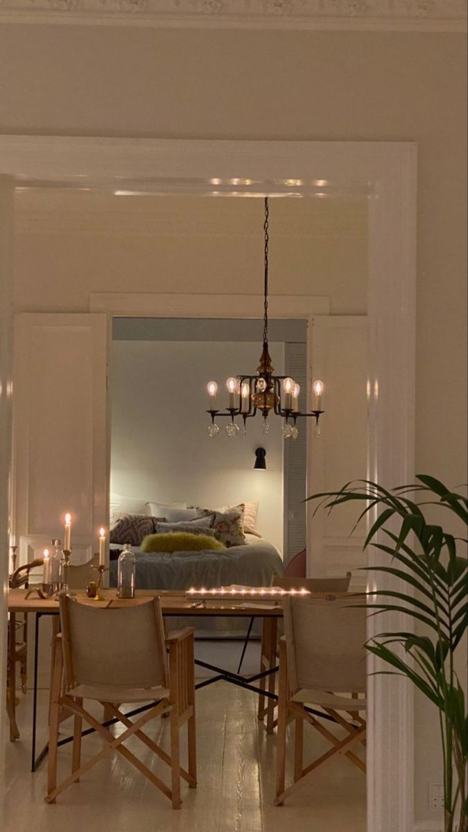 a dining room table and chairs in front of a bed with chandelier hanging from the ceiling