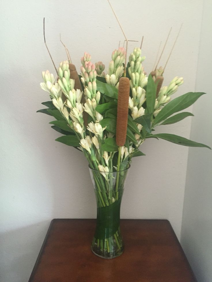 a vase filled with white flowers sitting on top of a wooden table next to a wall