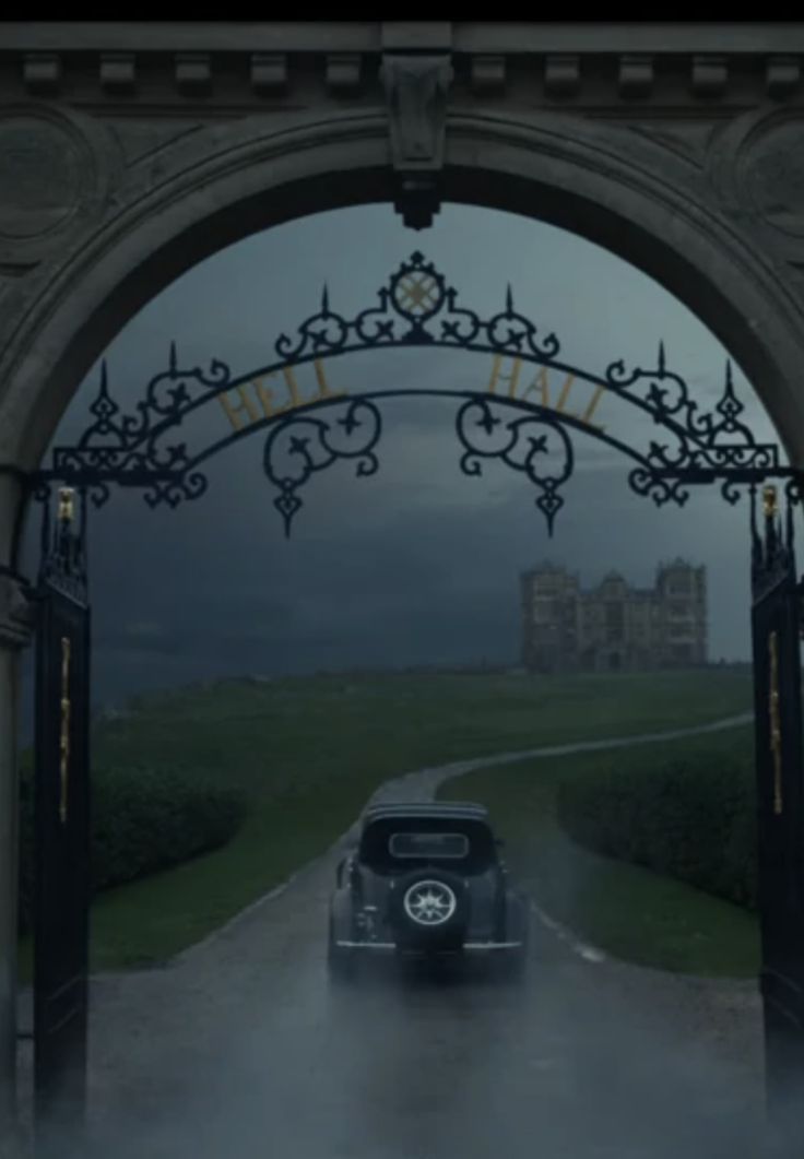 an old black car driving through a gated entrance to a castle in the rain