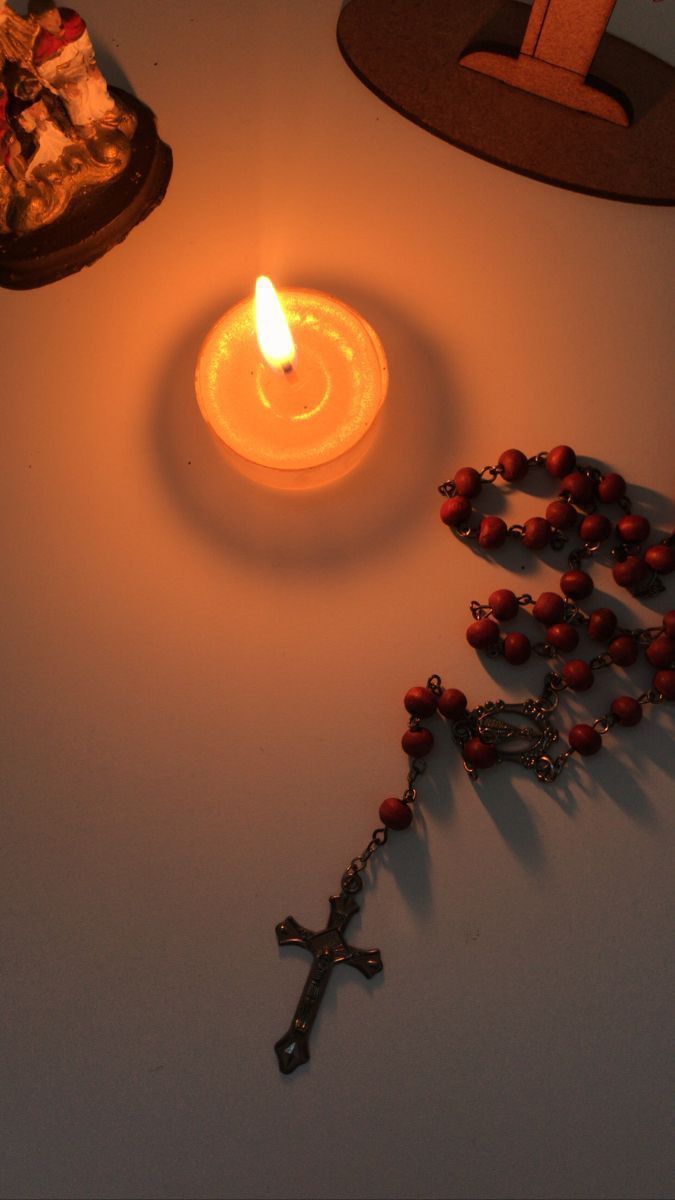 a lit candle sitting next to a rosary on a table with other items around it