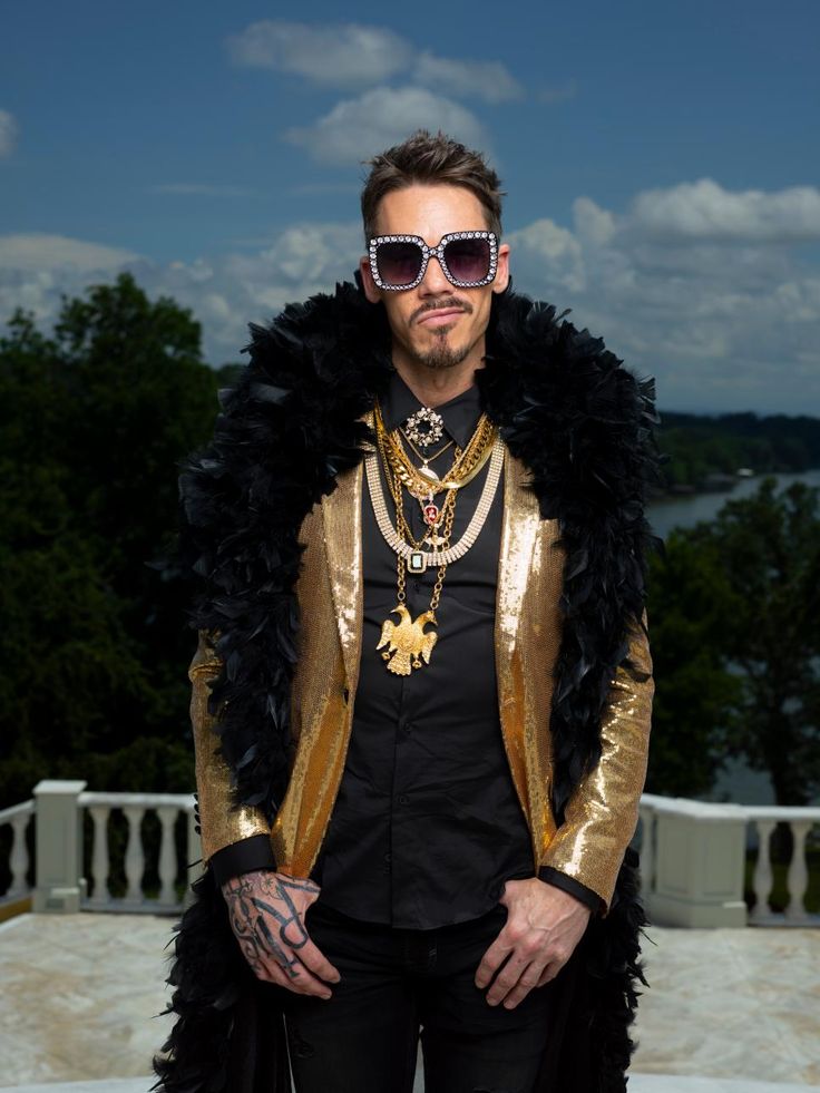 a man in a gold and black jacket with his hands on his hips wearing sunglasses