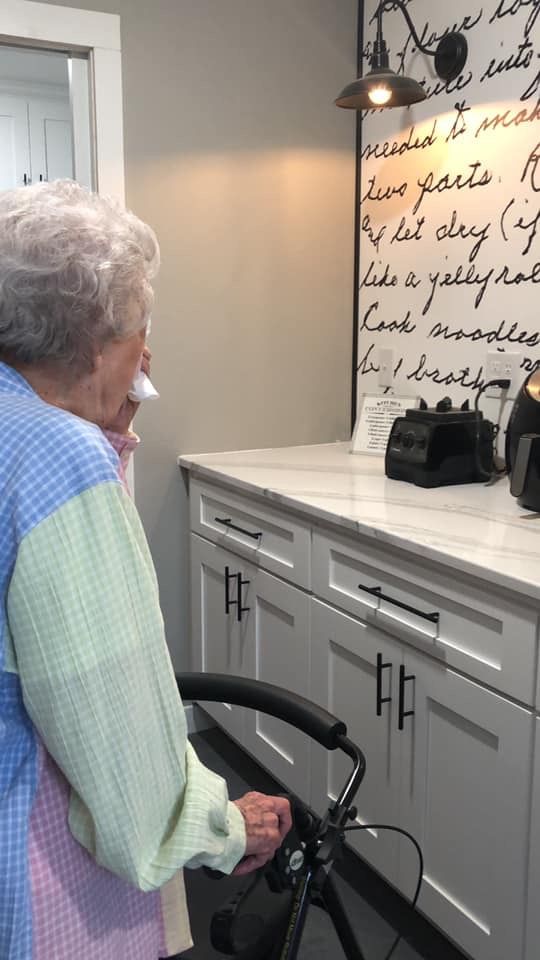 an elderly woman standing next to a bicycle in a kitchen area with writing on the wall