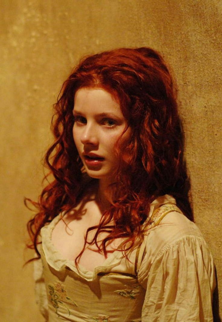 a woman with long red hair standing next to a wall