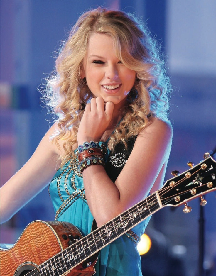 a woman holding a guitar while standing in front of a microphone and wearing a blue dress