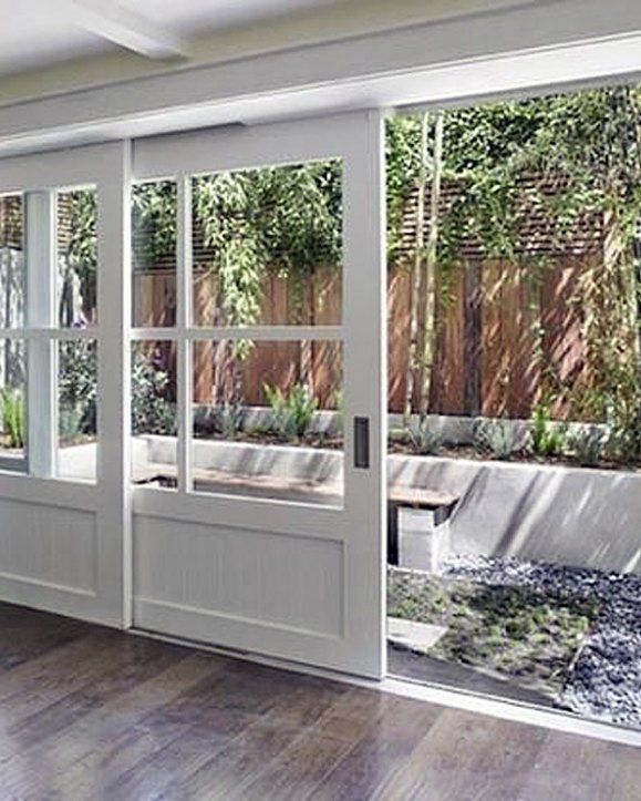 an empty room with sliding glass doors and wood flooring in the center, looking out onto a garden