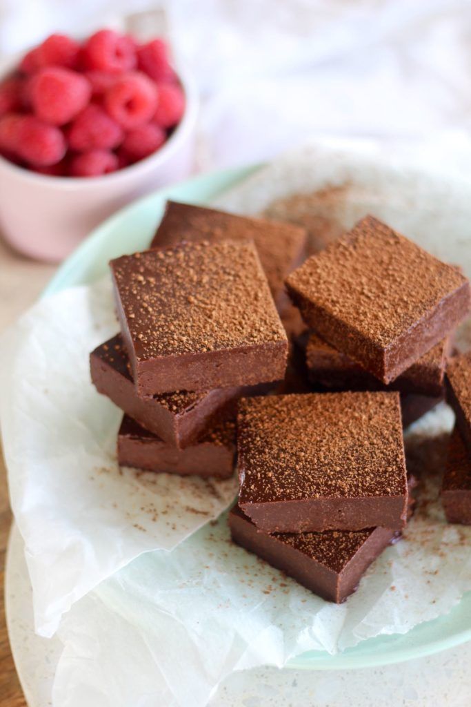 there are many pieces of brownies on the plate with raspberries in the background