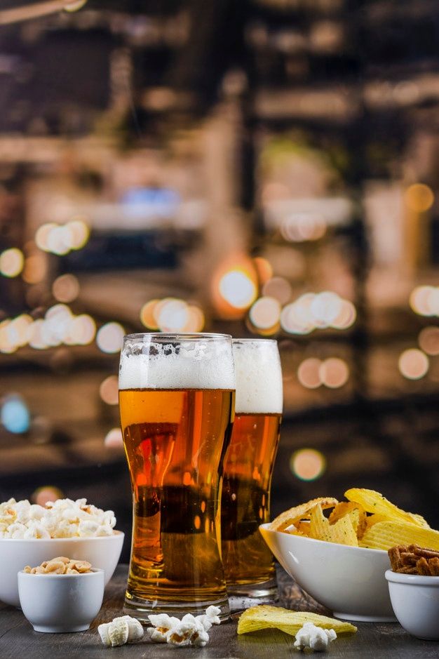 two glasses of beer and bowls of food on a table