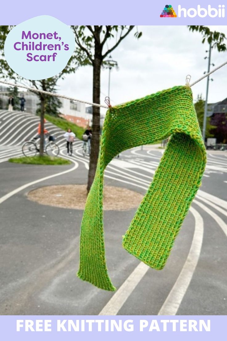 a green knitted scarf hanging from a tree in the middle of a street with text overlay that reads, free knitting pattern money, children's scarf