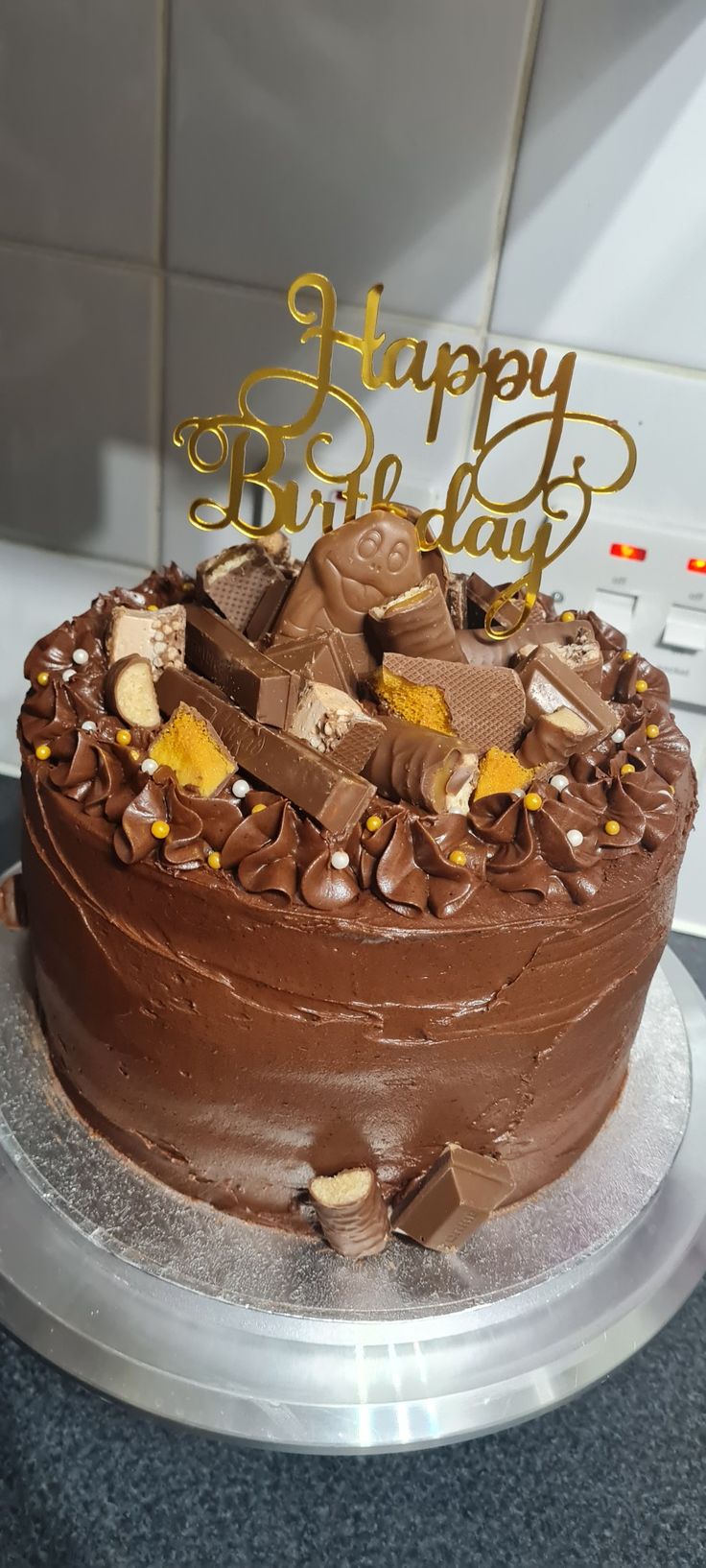 a birthday cake with chocolate frosting and gold letters on top that says happy birthday