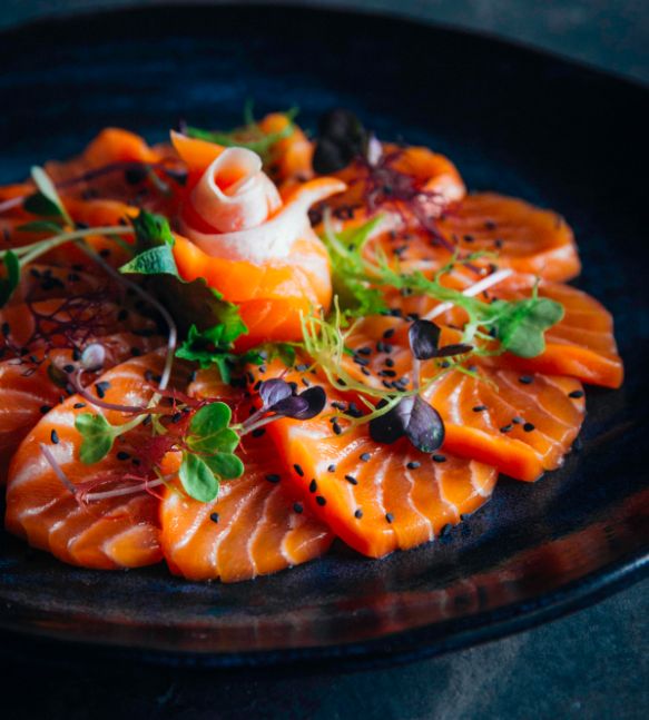 a black plate topped with sliced up salmon and veggies on top of it