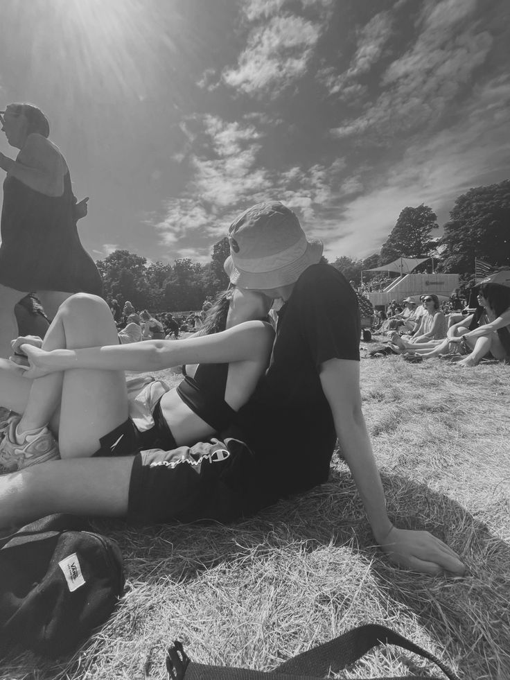 black and white photograph of people sitting on the ground at an outdoor event, with one person holding onto another woman's leg