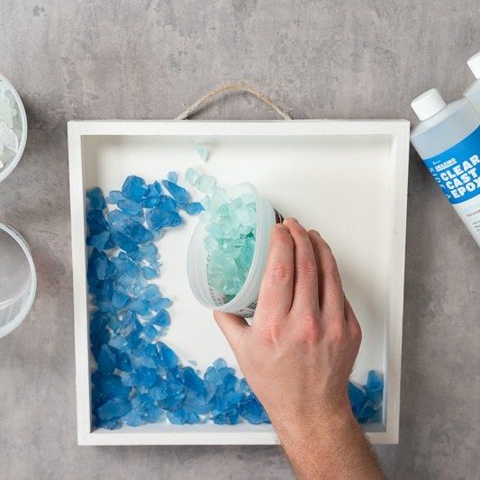 a person is using blue and white sea glass to decorate a tray with water bottles