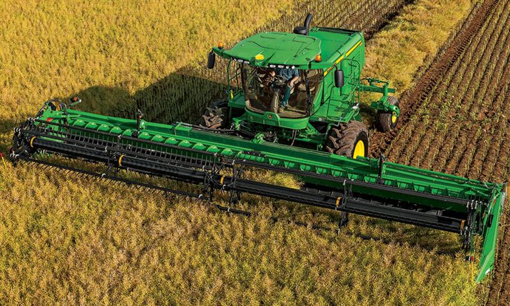 a large green tractor driving through a lush green field next to a couple of rows of crops