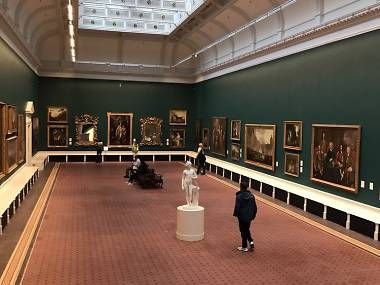 people are looking at paintings on display in a large room with red carpeted flooring