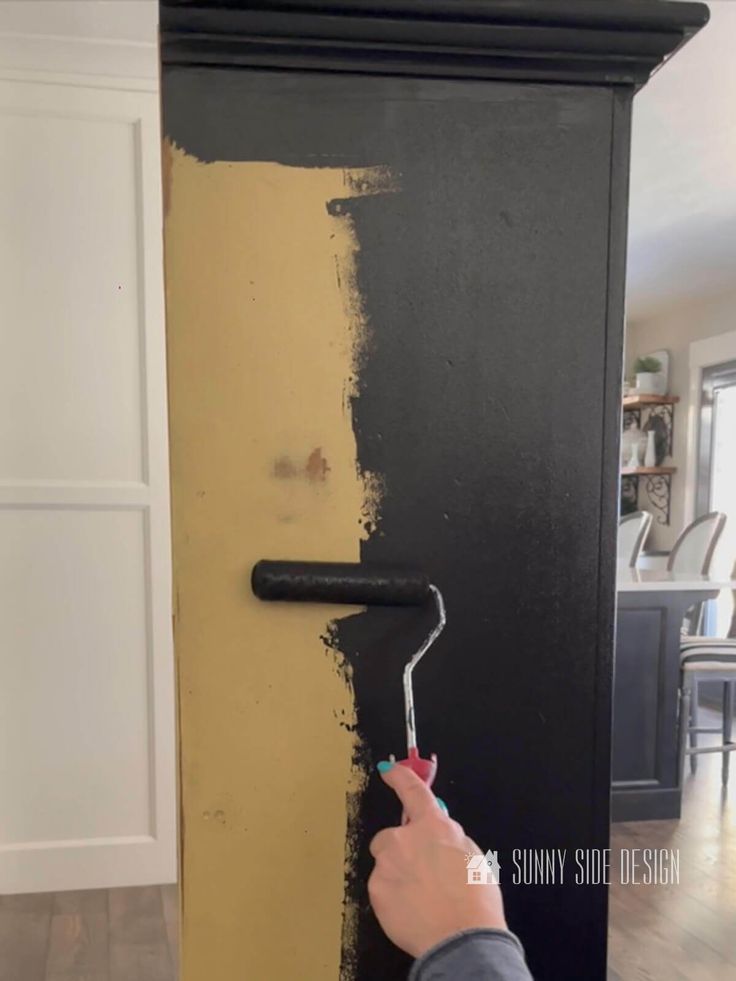 someone is painting the side of a black cabinet with yellow paint and a white brush