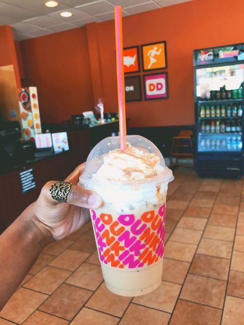 a hand holding up a drink in a cup with whipped cream and toppings on top