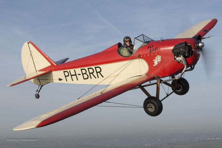 a small red and white plane flying in the sky with two men sitting inside it