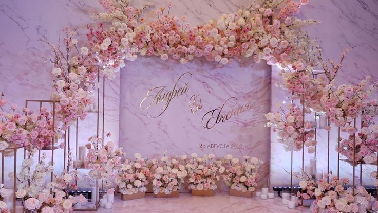 an elegant wedding setup with pink flowers and gold lettering on the wall, along with candles