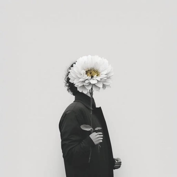 a man with a flower on his head standing in front of a white wall and looking at the sky