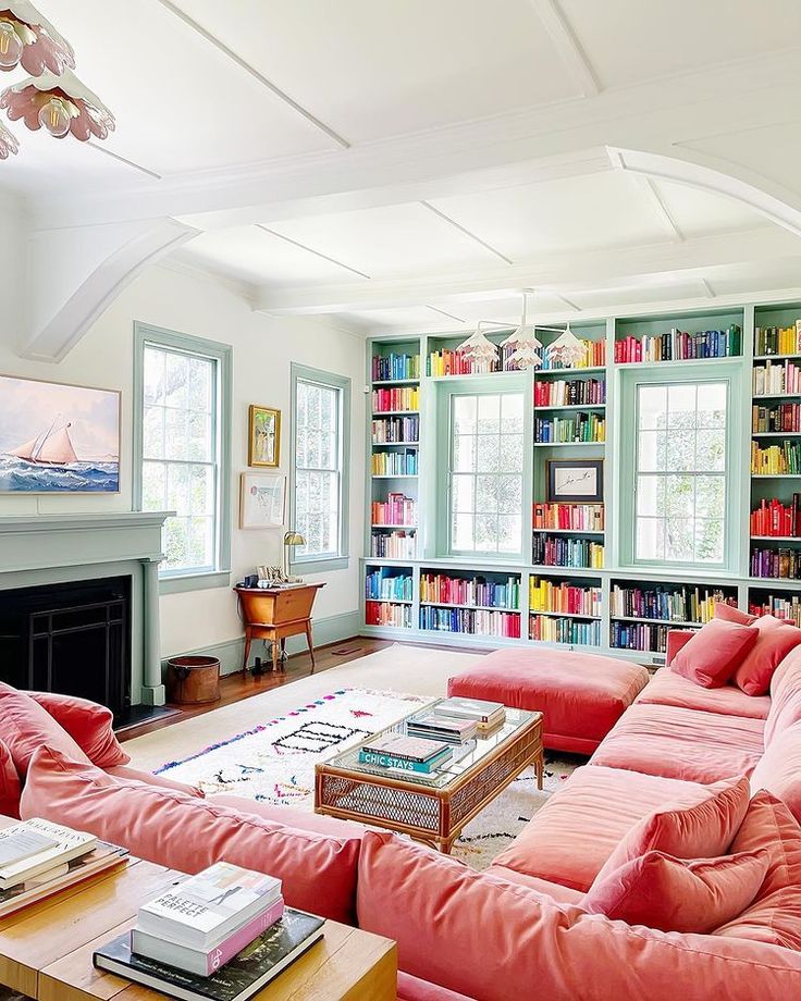 a living room filled with pink couches and bookshelves next to a fire place