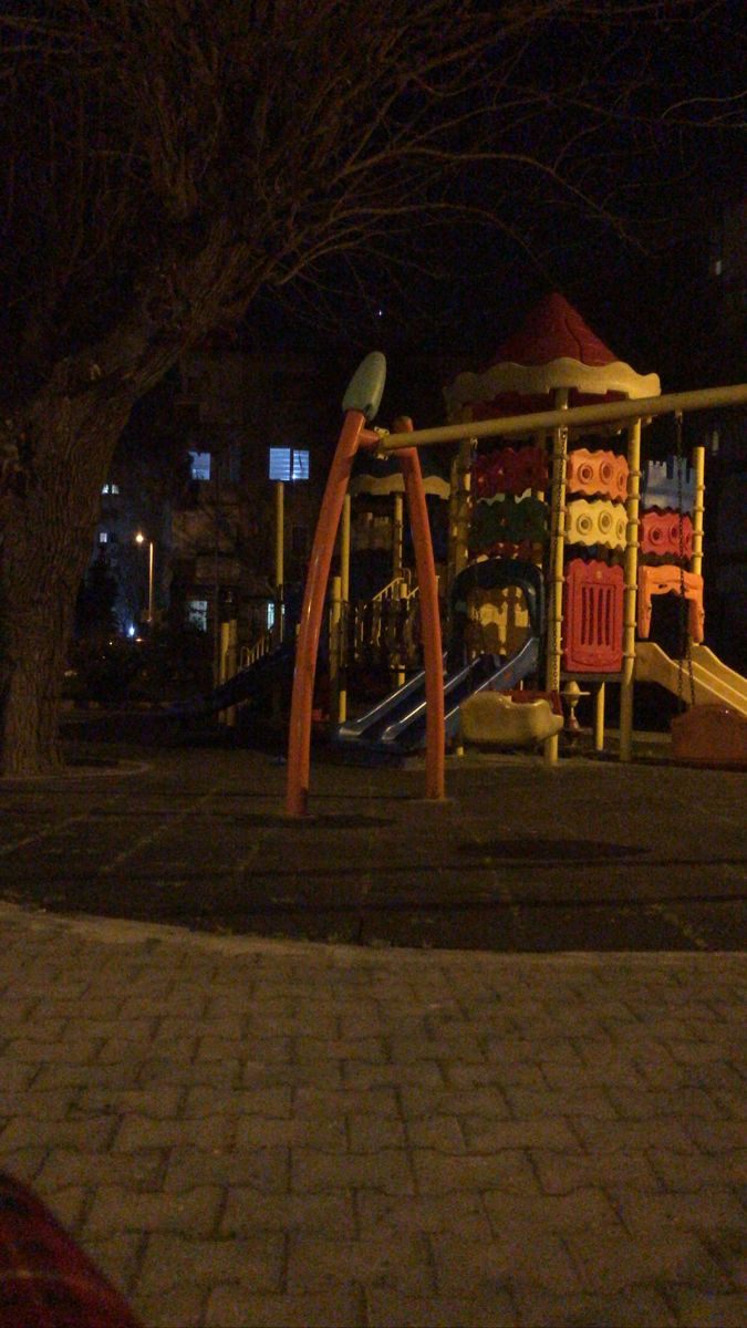 a child's play area at night with swings and slides in the background,