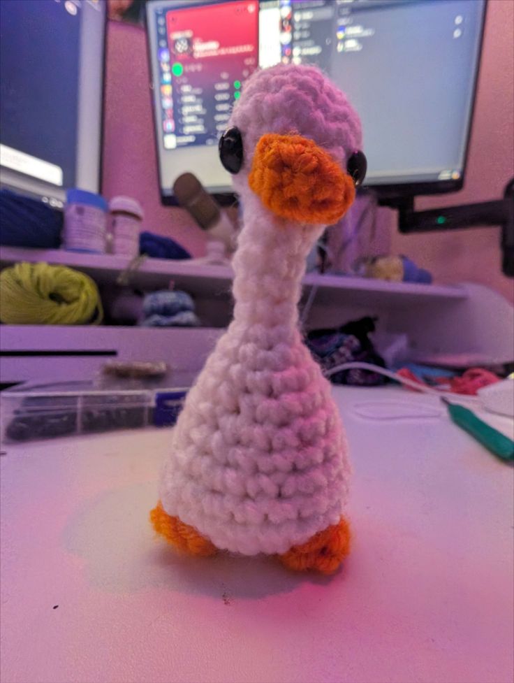 a crocheted bird sitting on top of a table next to a computer monitor