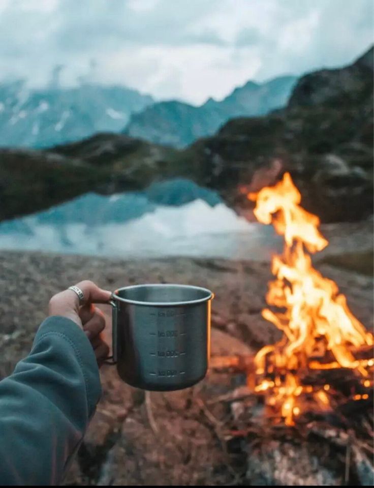 a person holding a cup in front of a campfire