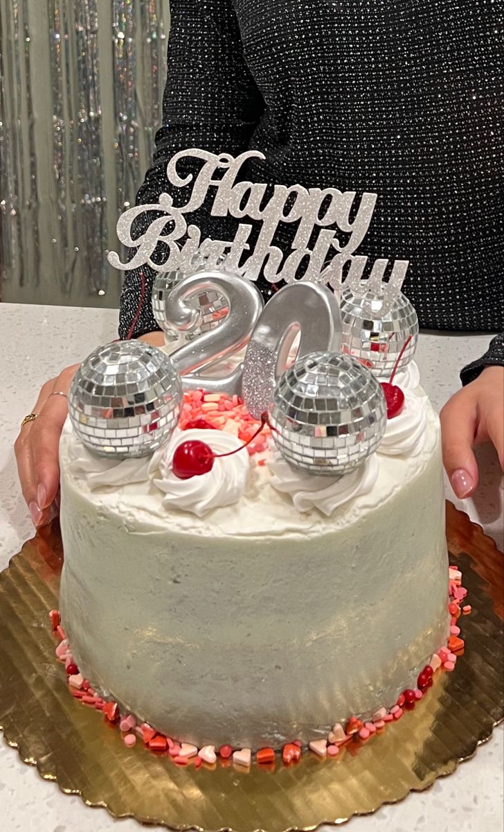 a person holding a cake with the number twenty on it and two disco ball decorations