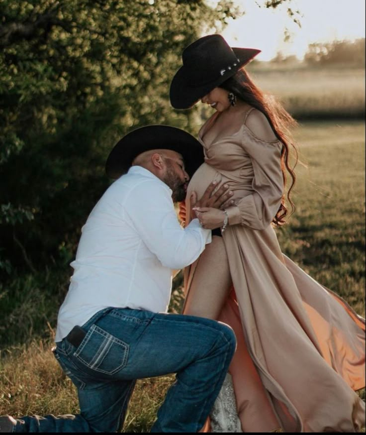 a man kneeling down next to a woman in a dress and cowboy hat on the ground