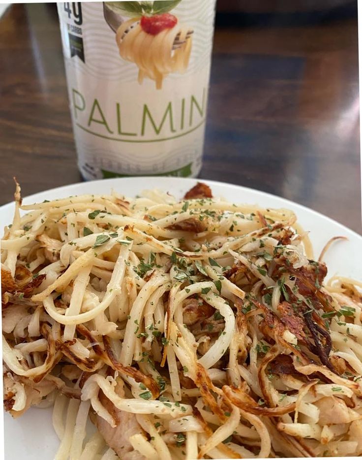 a white plate topped with pasta covered in parmesan cheese and herbs next to a bottle of wine