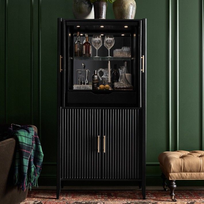 a black cabinet with wine glasses and bottles on it in front of a green wall