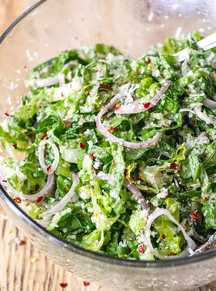 a salad in a glass bowl with onions and lettuce on the side, ready to be eaten